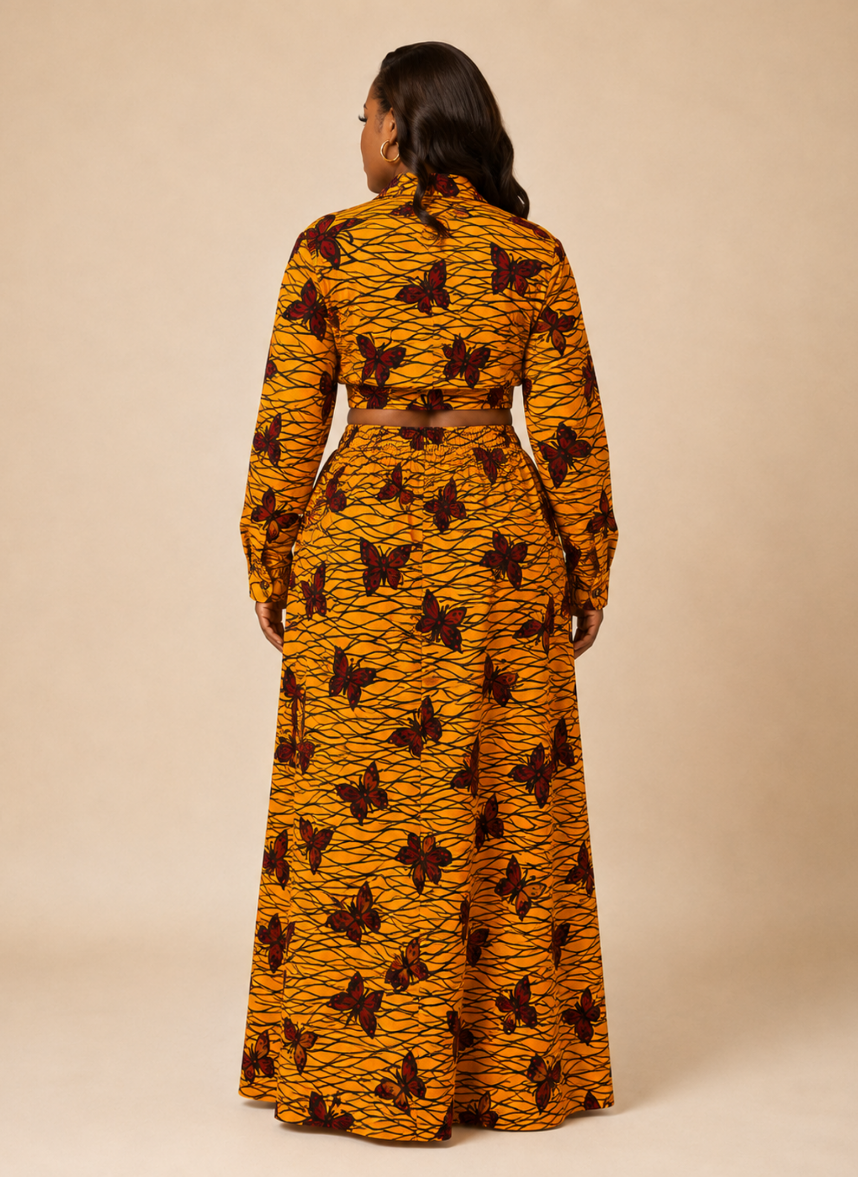 A woman viewed from the back wearing a long-sleeve, high-neck maxi dress with a mustard yellow and dark brown abstract pattern, set against a solid beige studio background.