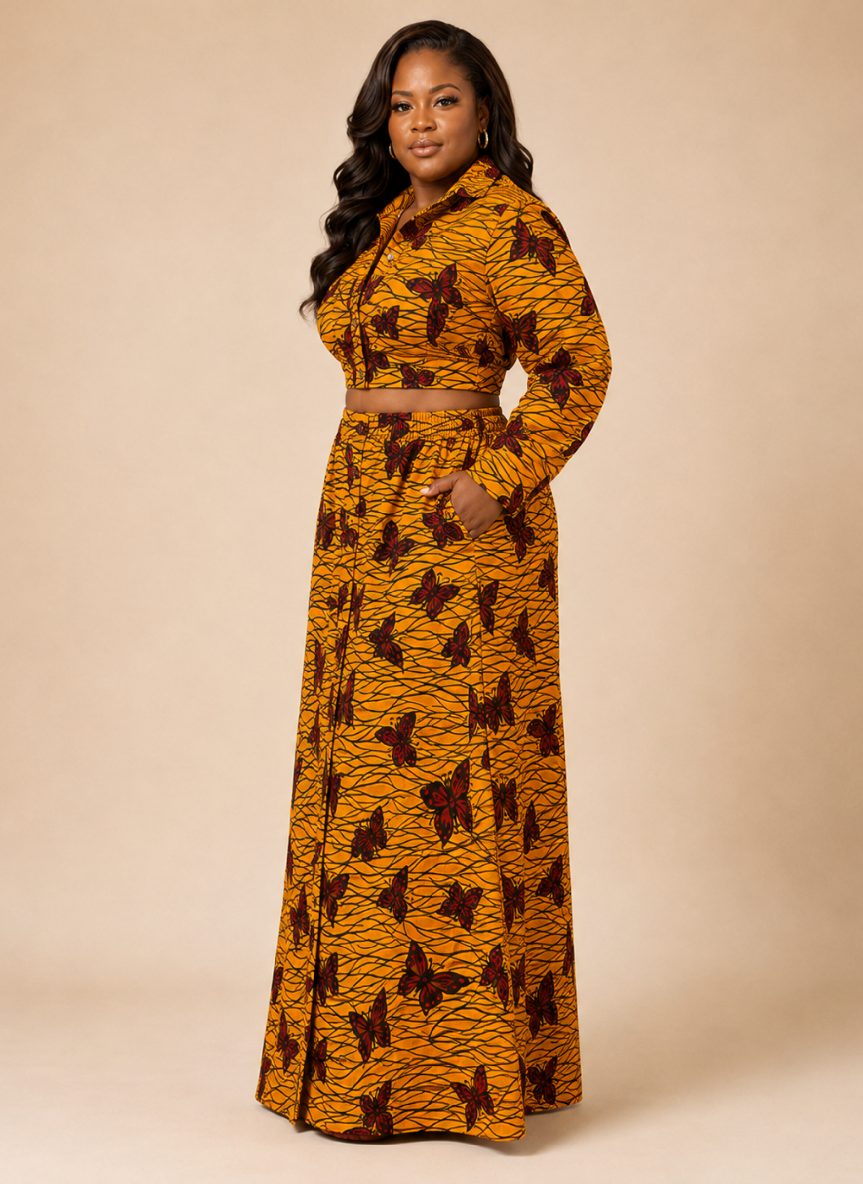A woman modeling a long-sleeve, collared, belted maxi dress with a mustard yellow and brown abstract pattern, set against a solid beige studio background.