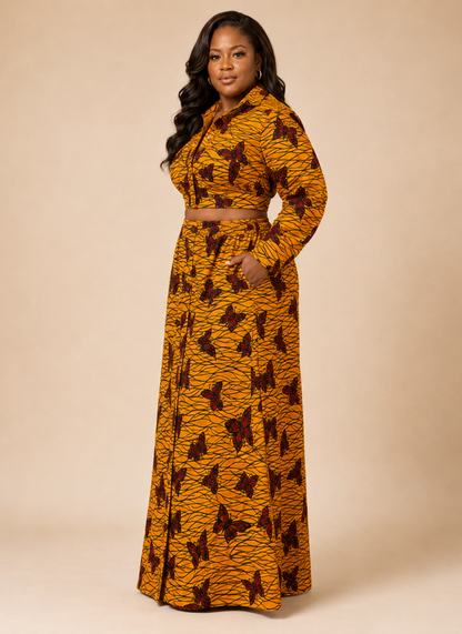 A woman modeling a long-sleeve, collared, belted maxi dress with a mustard yellow and brown abstract pattern, set against a solid beige studio background.