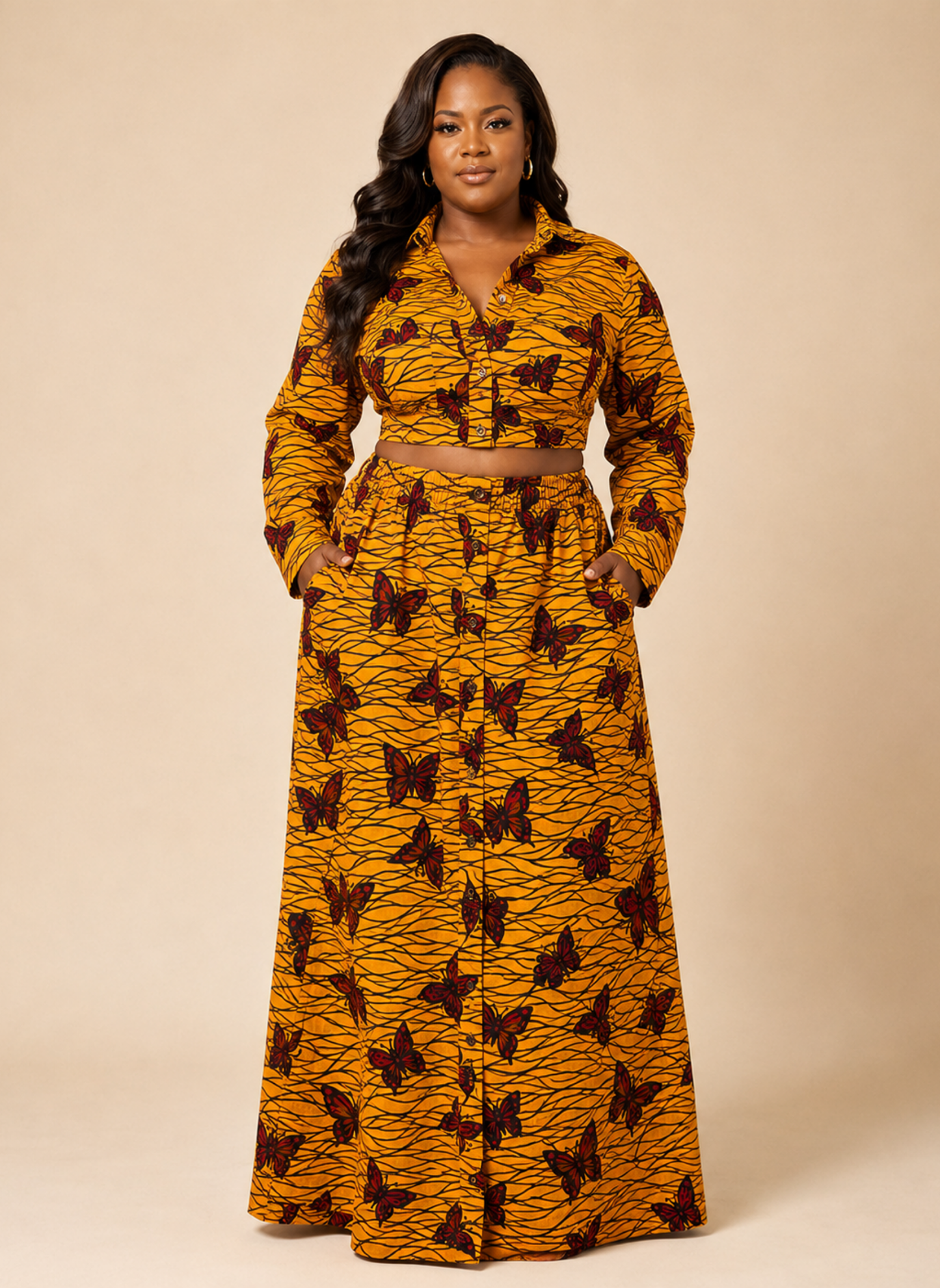 A woman modeling a long-sleeve, button-front maxi dress with a matching waist belt. The dress features a vibrant mustard yellow and orange tiger-stripe pattern with dark brown butterfly prints, set against a solid beige studio background.