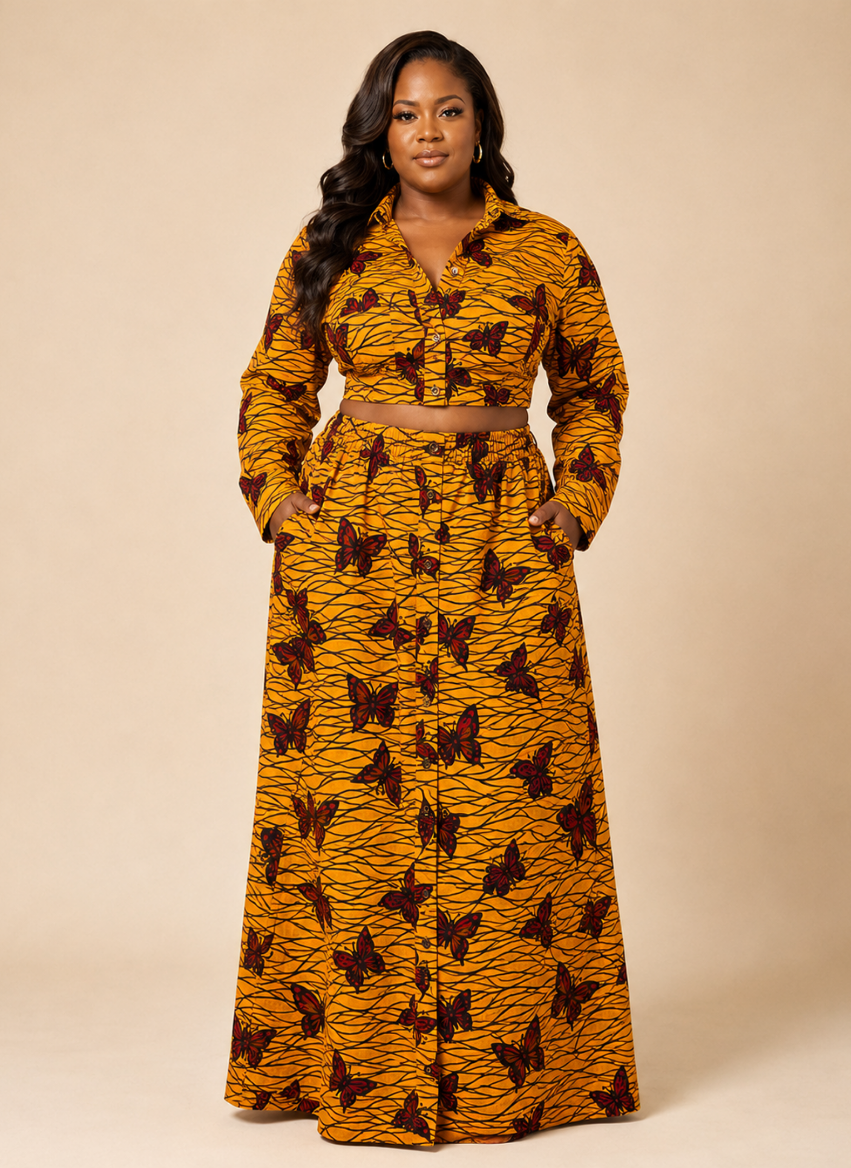 A woman modeling a long-sleeve, button-front maxi dress with a matching waist belt. The dress features a vibrant mustard yellow and orange tiger-stripe pattern with dark brown butterfly prints, set against a solid beige studio background.