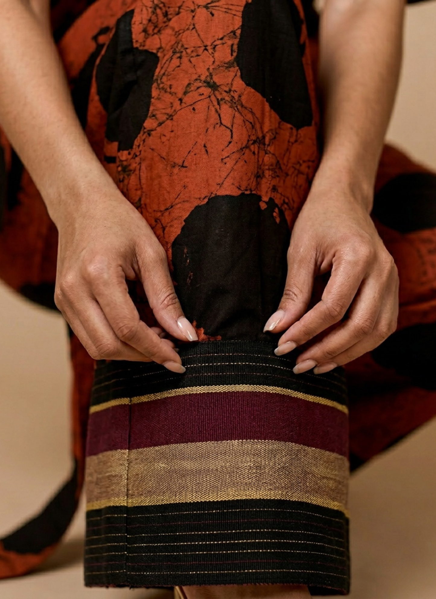 Person holding a striped bag with an orange and black patterned garment in the background