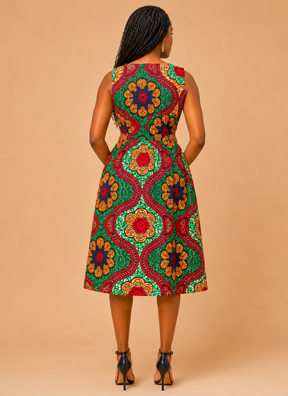 A woman viewed from behind wearing a sleeveless A-line midi dress with a vibrant, multicolored African wax print featuring red, green, orange, and yellow geometric and floral motifs. She is standing against a solid beige studio background.