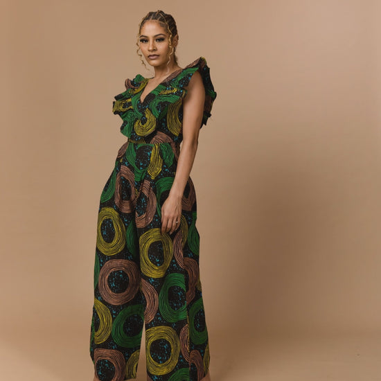 Side profile of a model walking in a luxury Ankara jumpsuit showcasing the architectural shoulder ruffle